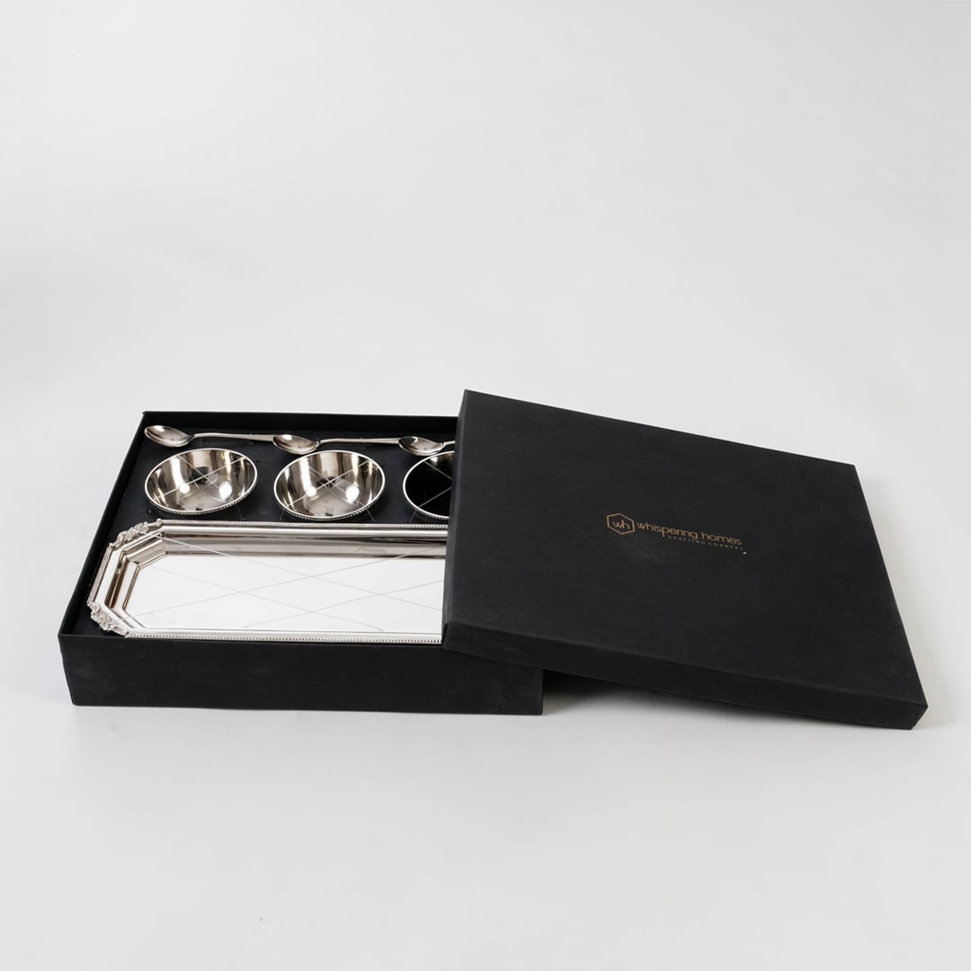 Silver condiment set presented in an open black gift box on a white background highlighting the polished bowls spoons and tray in a premium layout.
