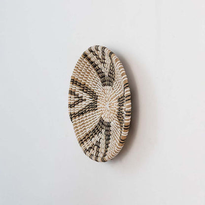 Round wicker wall decor plate handmade with natural brown black and white weaving side view image perfect for modern decor.