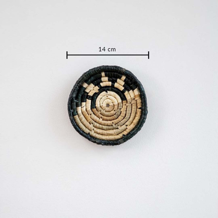 Handwoven round wall basket in black and natural fiber showing approx 25 cm diameter for accurate interior wall decor placement.