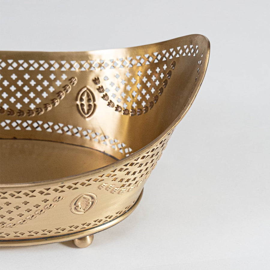 Decorative gold metal fruit bowl with rounded feet and perforated curved body displayed on white background surface.