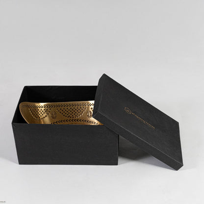 Side-angled view of gold metal fruit bowl with curved upward edges and cutout design shown on plain white backdrop.
