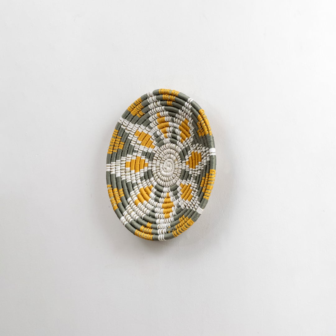 Side angled view of a handcrafted woven wall plate showing its raised textured weaving pattern and natural material detailing.