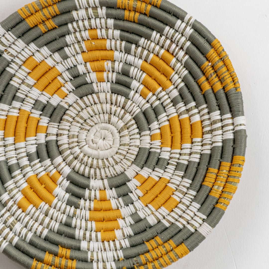 Closeup view of a handcrafted woven wall plate revealing intricate weaving details natural fibers and color transitions between mustard green cream and white sections.