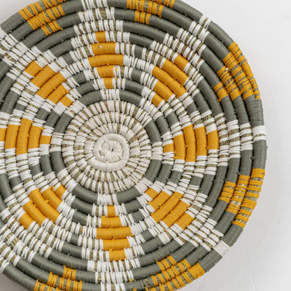 Closeup view of a handcrafted woven wall plate revealing intricate weaving details natural fibers and color transitions between mustard green cream and white sections.