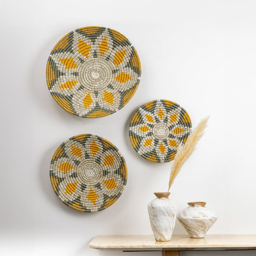 Colorful handcrafted woven wall plates displayed on a white background with three decorative vases placed on a wooden table creating a warm lifestyle setting.