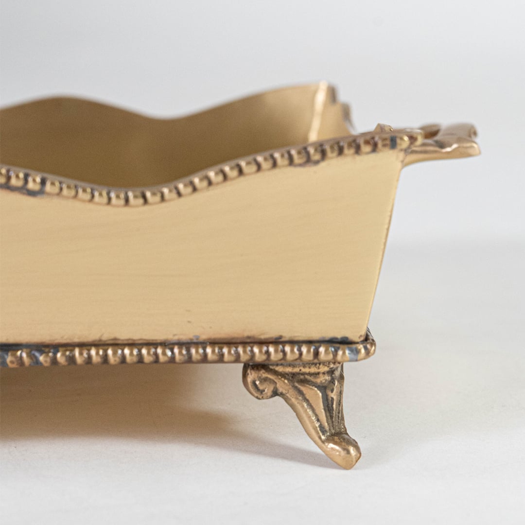 A closeup view of a gold decorative serving tray showing its detailed embossed pattern and elegant raised edging with a refined metallic finish.