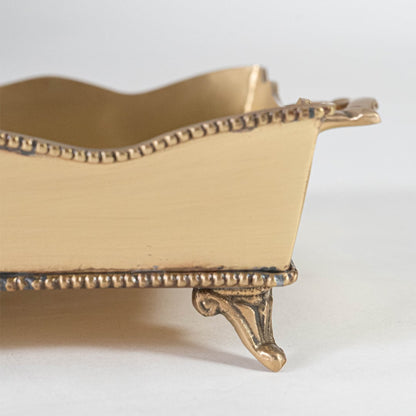 A closeup view of a gold decorative serving tray showing its detailed embossed pattern and elegant raised edging with a refined metallic finish.