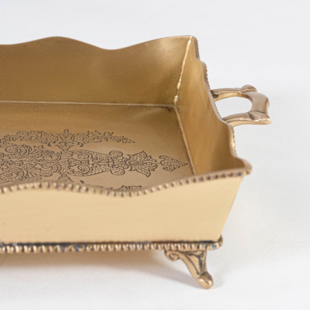 Side closeup of gold brass tray showing engraved base ornate edge detailing and antique style handle on white.