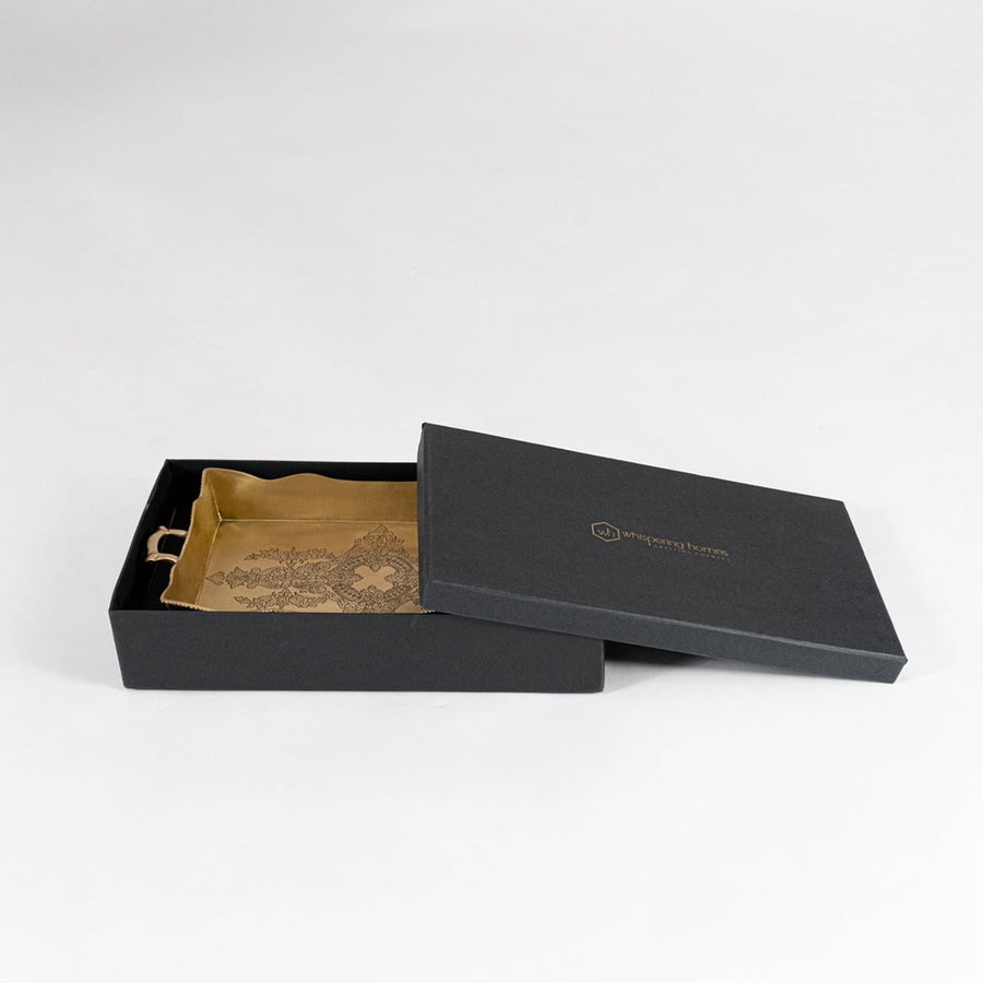 Gold brass serving tray partially packed inside elegant black box with gold logo branding placed on white surface.