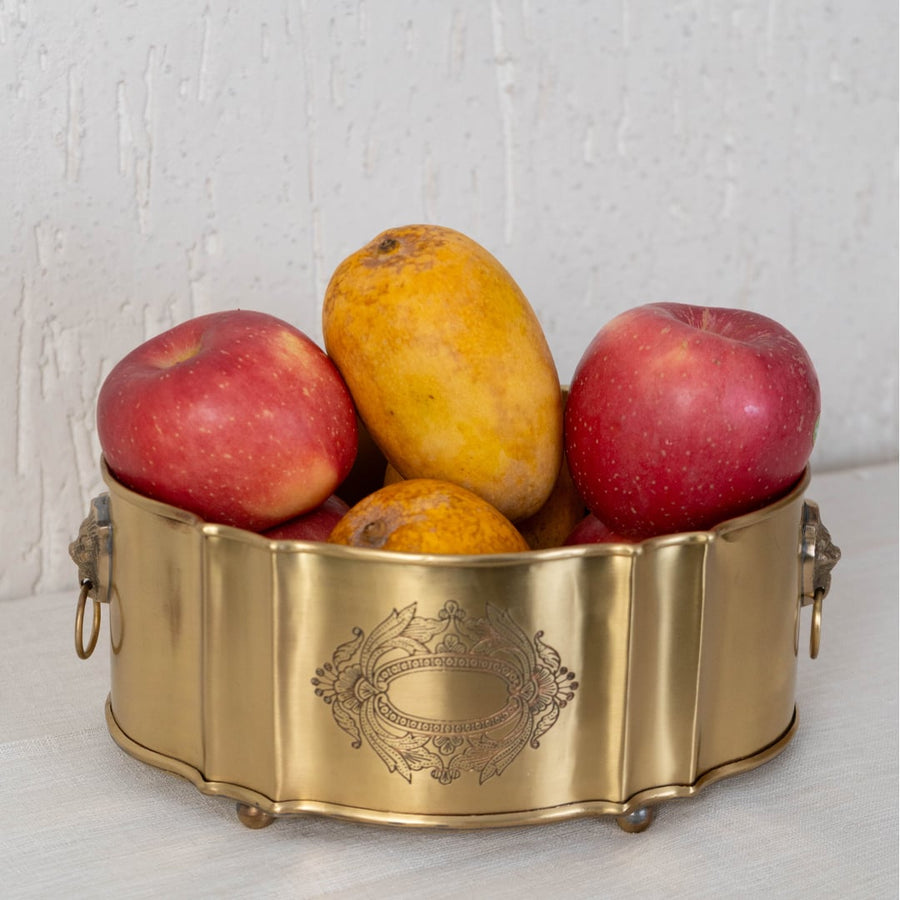 Top view of empty gold brass container with wavy edge and lion ring handles displayed on white background.