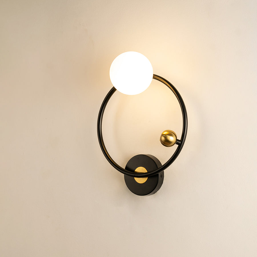 Elegant black and gold metal wall light with frosted globe shade mounted on white wall for modern home decor inspiration.