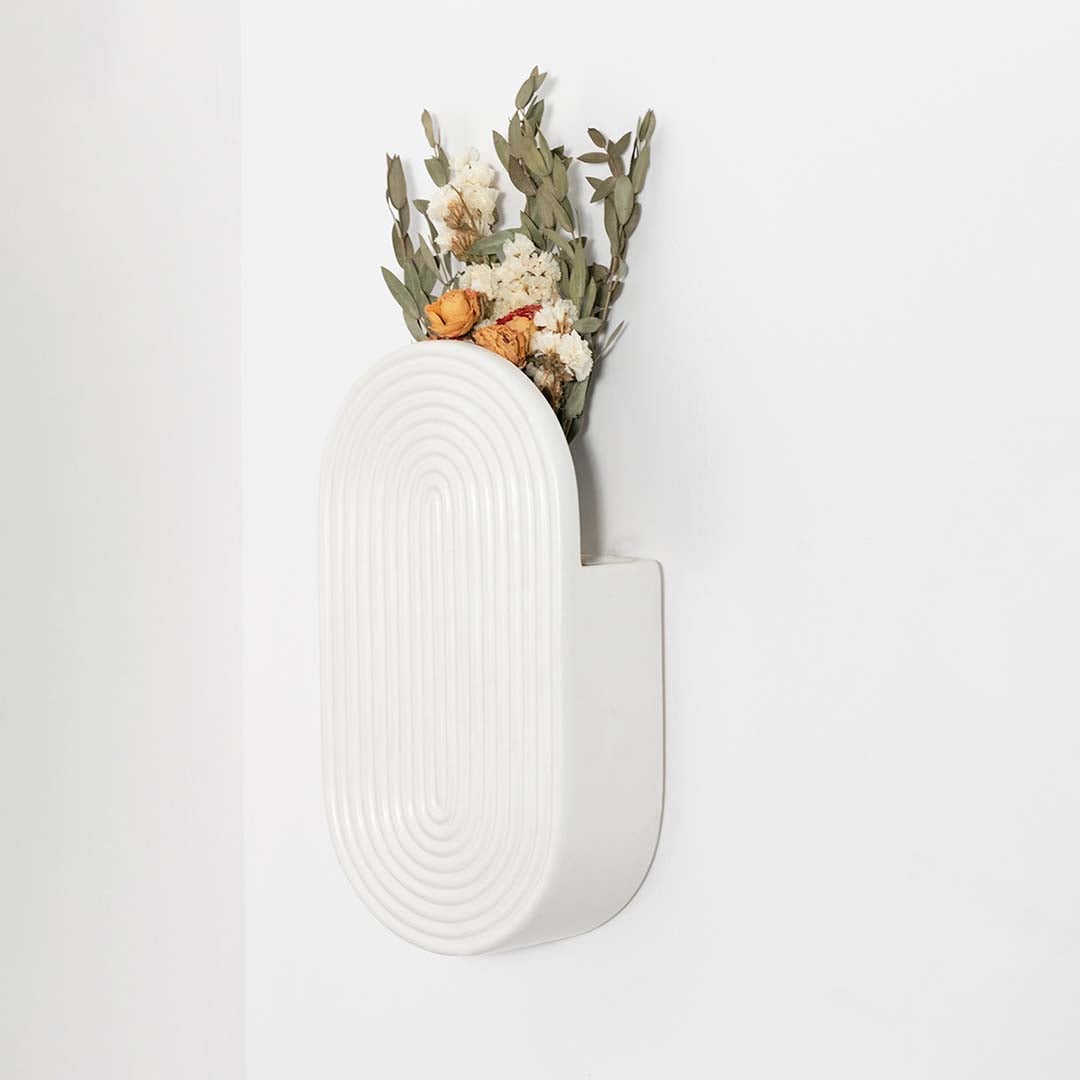 Minimal white ceramic wall vase displayed on a clean backdrop highlighting its curved textured modern form.
