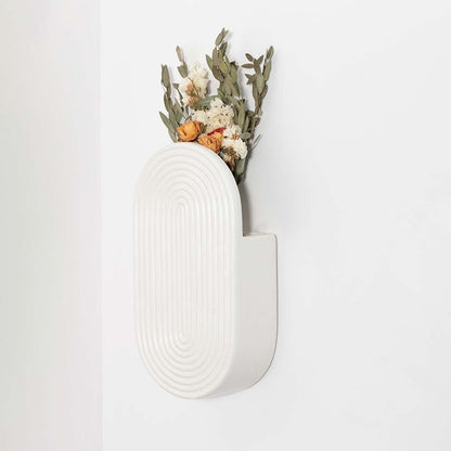 Minimal white ceramic wall vase displayed on a clean backdrop highlighting its curved textured modern form.