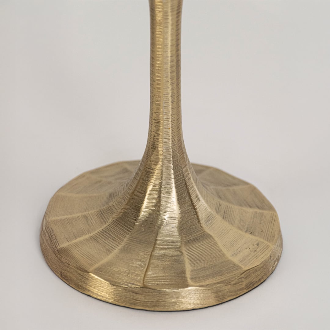 Close view of small gold candle holder highlighting detailed metal texture and wide sculpted base design in focus