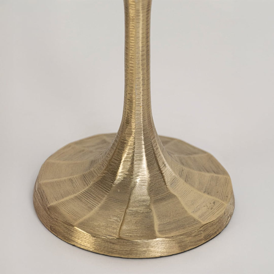 Close view of small gold candle holder highlighting detailed metal texture and wide sculpted base design in focus