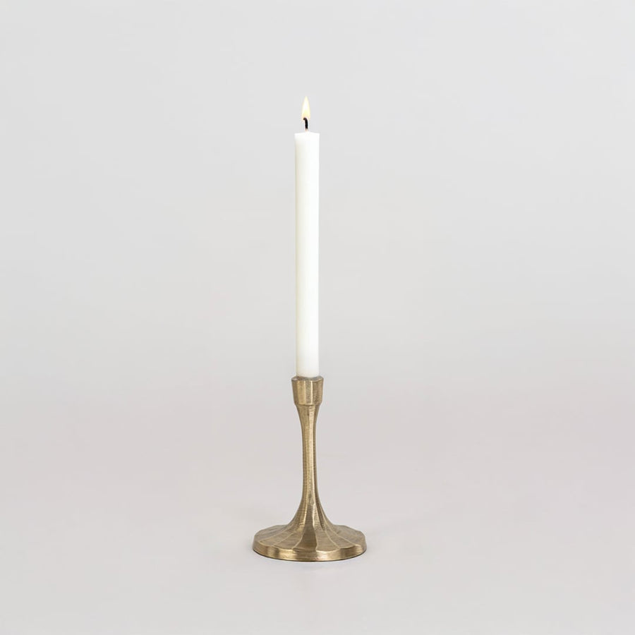 Short gold metal candle holder with sculpted base and smooth finish shown clearly on bright white background wall