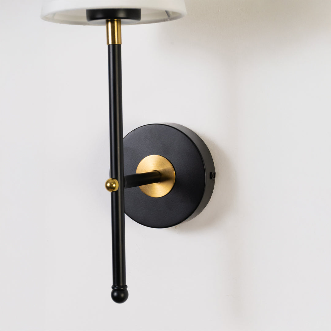 Elegant wall light in black and gold metal finish with cylindrical arm for bedroom or living decor lighting placement white background.
