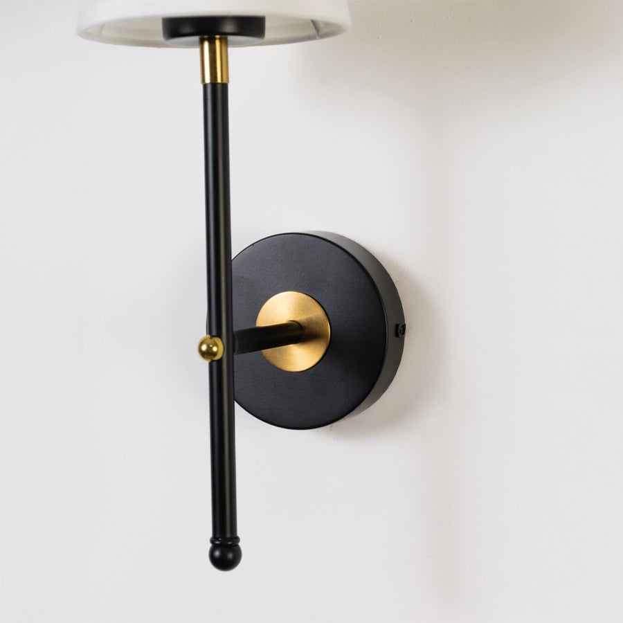 Elegant wall light in black and gold metal finish with cylindrical arm for bedroom or living decor lighting placement white background.
