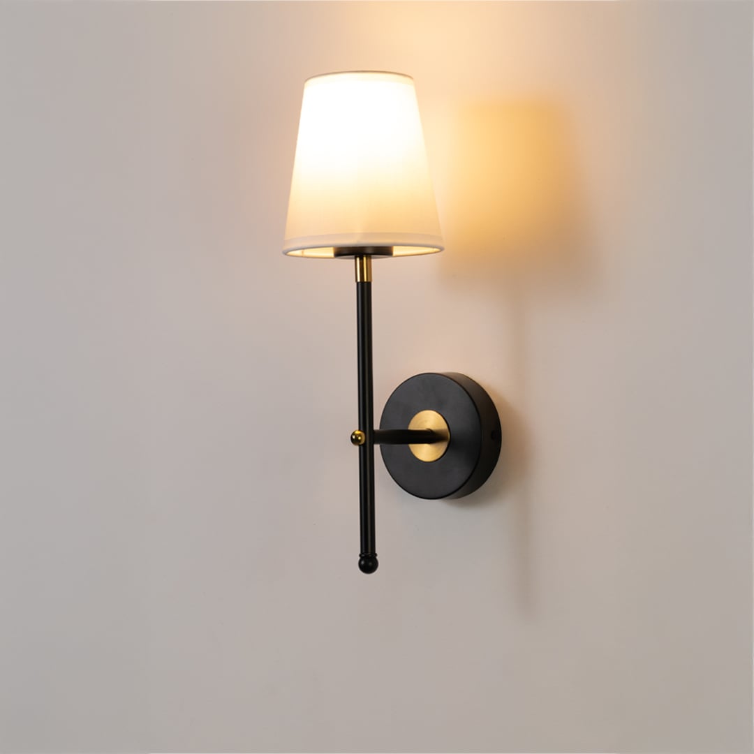Black metal wall light with white fabric shade and gold accents glowing softly on a clean white background ideal for modern indoor wall lighting.
