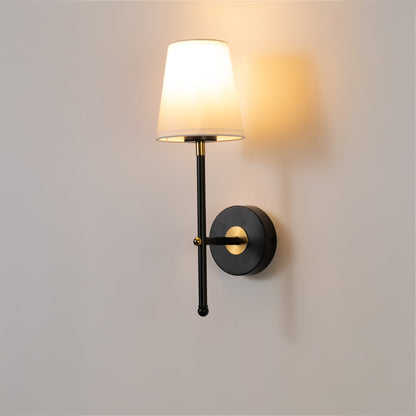 Black metal wall light with white fabric shade and gold accents glowing softly on a clean white background ideal for modern indoor wall lighting.