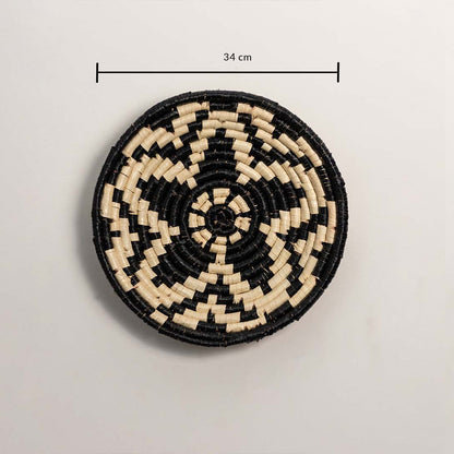 A handwoven natural and black rattan wall decor plate displayed on a white background clearly showing a diameter of 34 cm for accurate size reference and wall placement.
