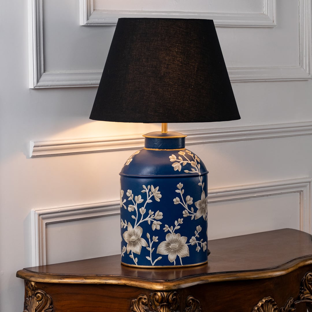 Table lamp with black fabric shade and deep blue ceramic base showcasing intricate floral and bird design placed on a wooden table against a white background.