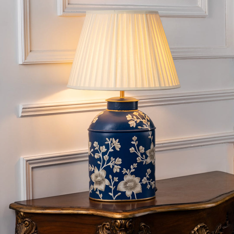 Table lamp on white background highlighting deep blue ceramic base with floral artwork and pleated shade offering classic luxury appeal.