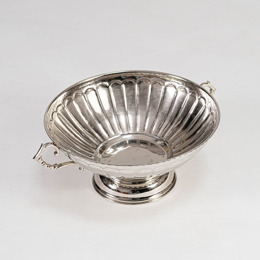 Shiny silver-toned fluted fruit bowl with curved handles on pedestal base placed on a plain white background.