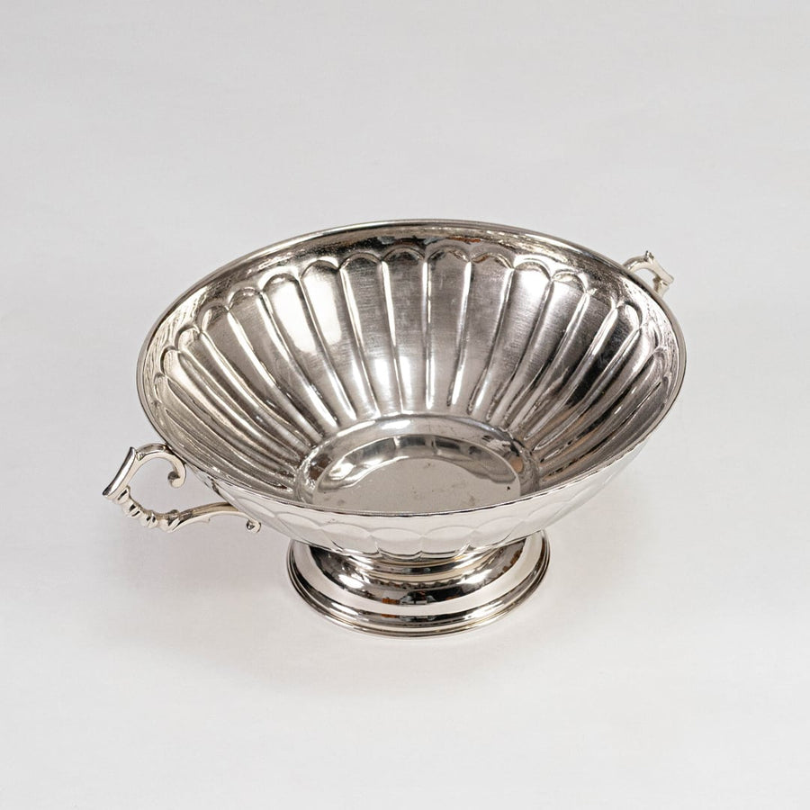 Shiny silver-toned fluted fruit bowl with curved handles on pedestal base placed on a plain white background.