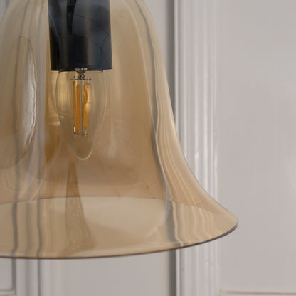 Closeup of amber glass pendant light with black metal fittings highlighting graceful curves and fine details.