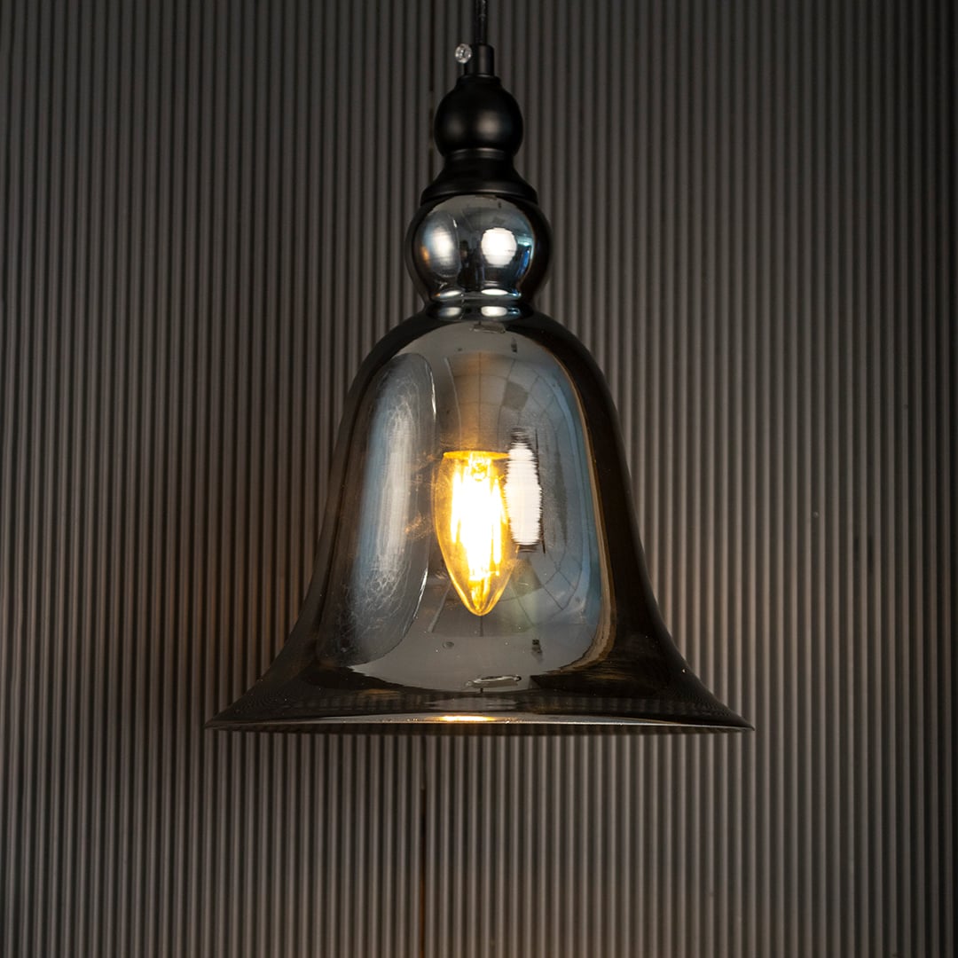 Glowing grey glass pendant lamp turned on suspended against a dark black background highlighting the warm light and bell shape.