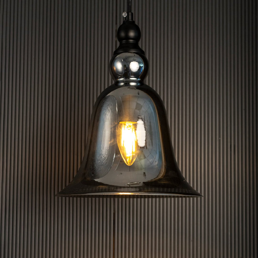 Glowing grey glass pendant lamp turned on suspended against a dark black background highlighting the warm light and bell shape.