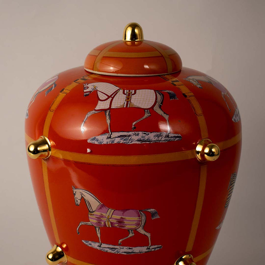 Red ceramic ginger jar with gold accents and lid placed on wooden surface against neutral background closeup highlighting luxury traditional decor appeal.
