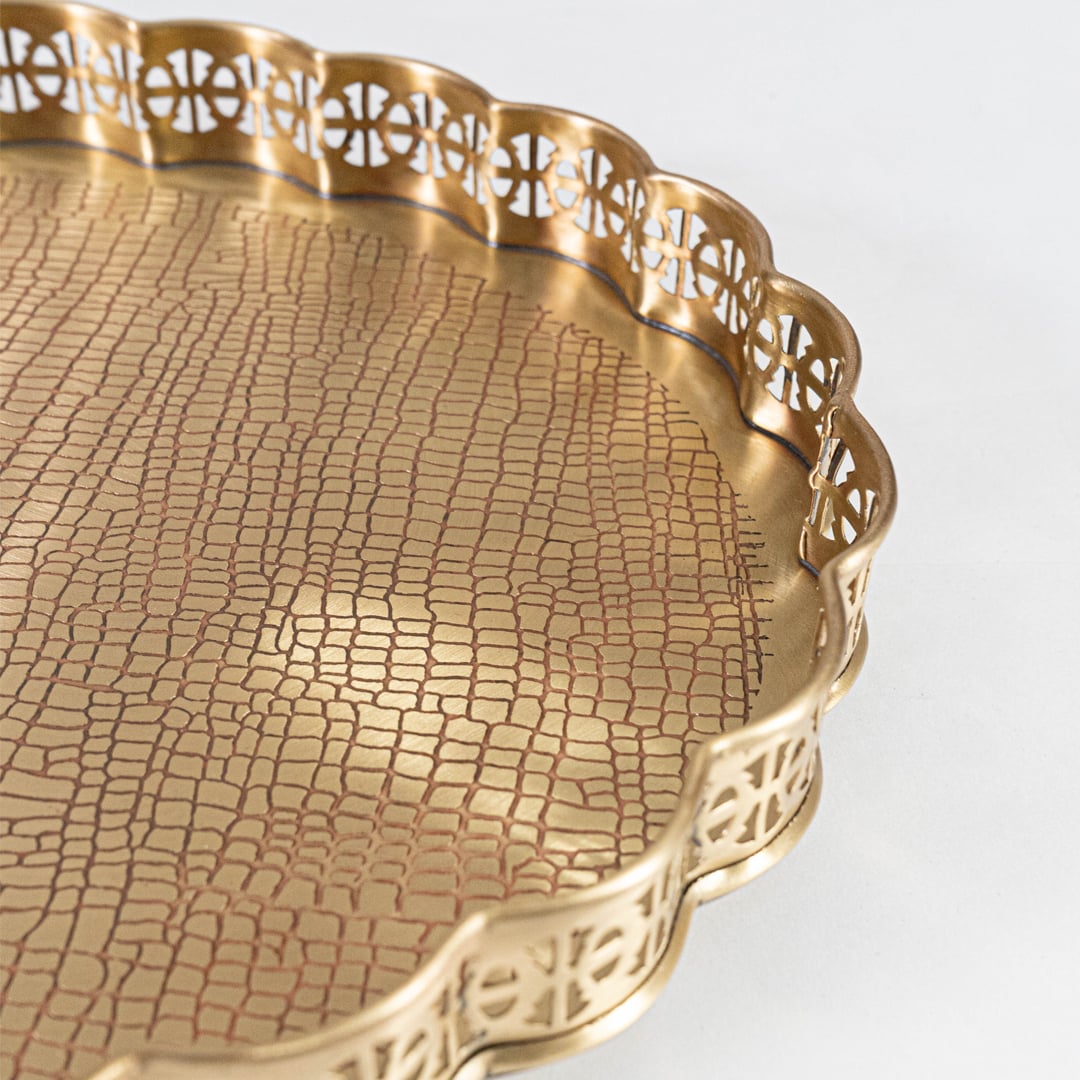 A closeup view of a golden serving tray showing detailed floral cutwork and smooth metal bowls filled with nuts capturing the fine texture and craftsmanship.