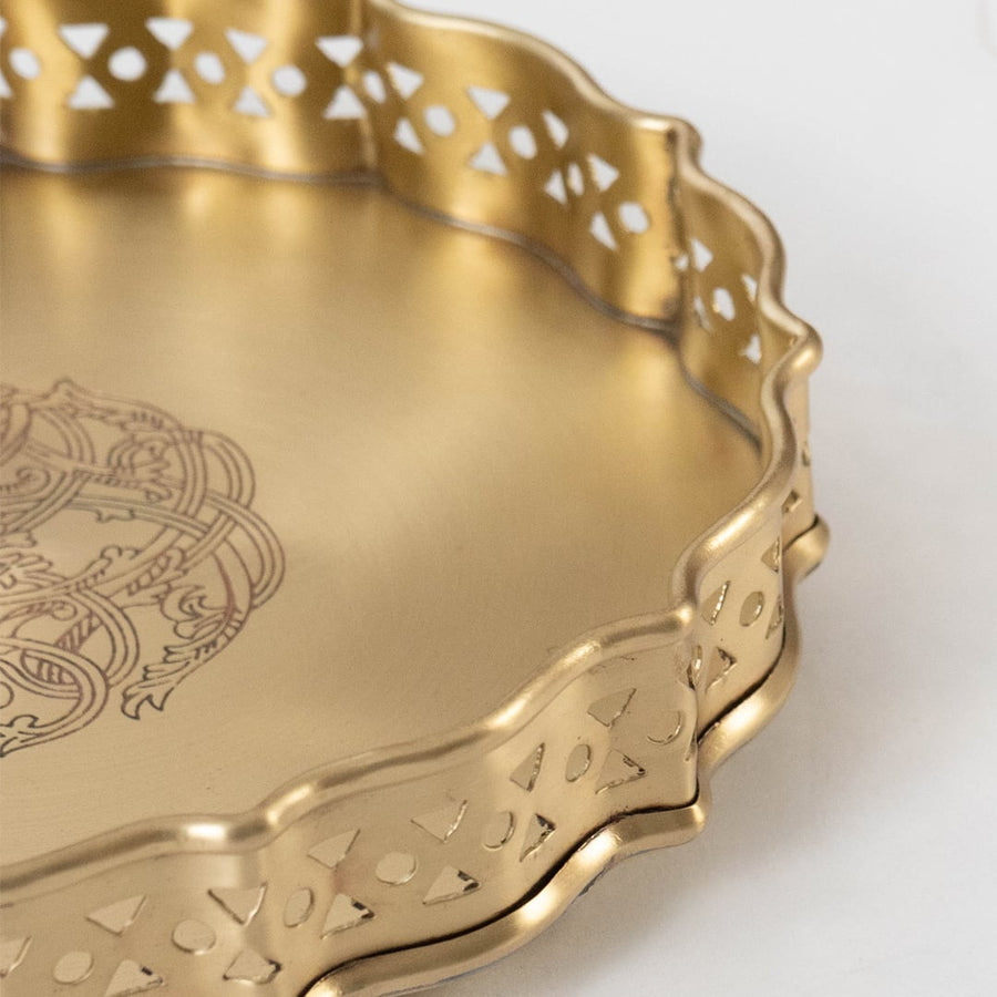 A closeup view of a gold serving tray showing the fine cutout patterns and smooth metallic bowls filled with snacks capturing the rich texture and craftsmanship.