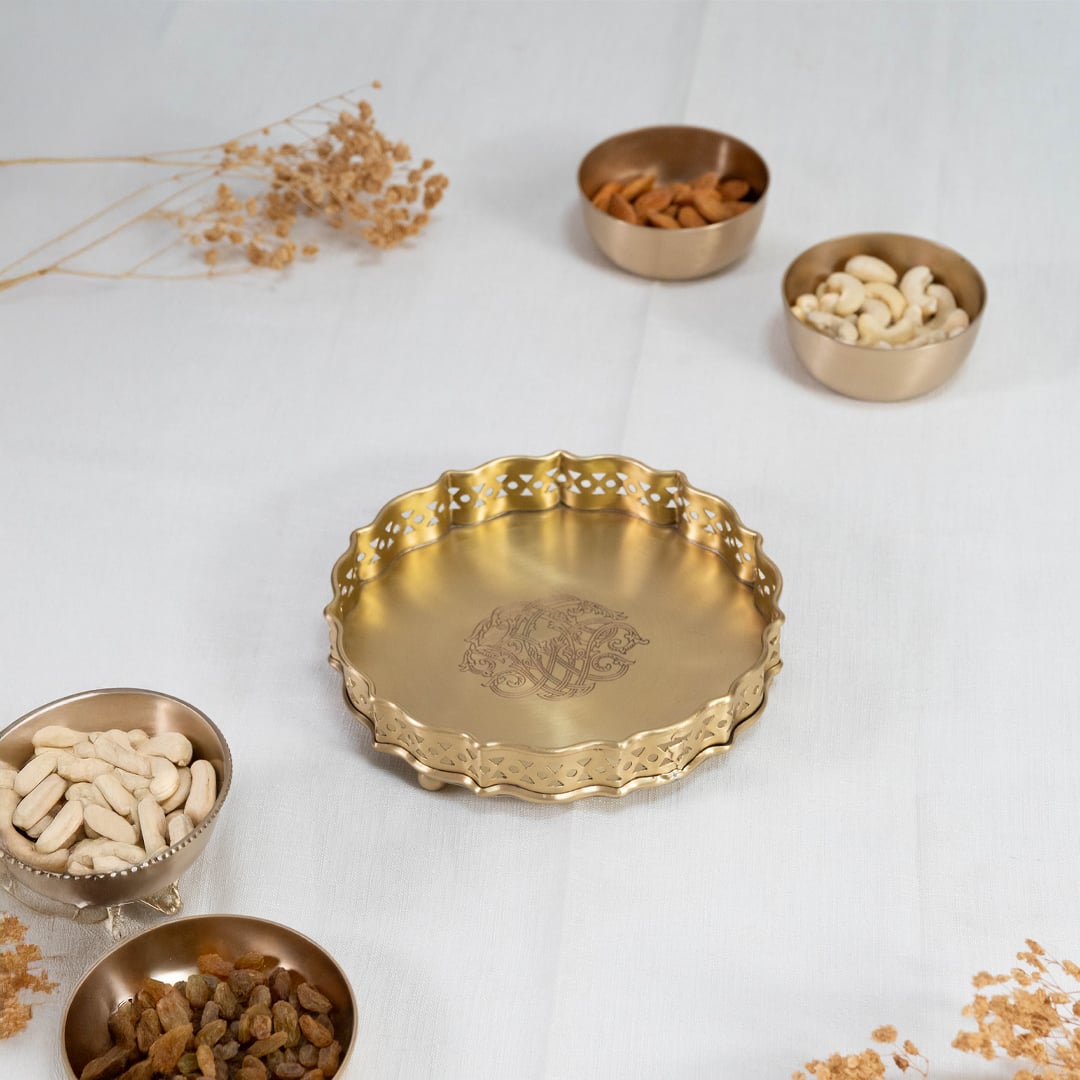 Decorative round brass plate in gold finish with scalloped edges and engraved floral design on white background.
