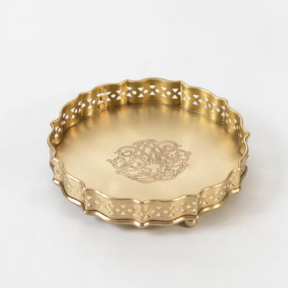 Decorative round brass plate in gold finish with scalloped edges and engraved floral design on white background.