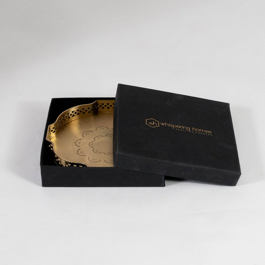 Gold brass plate partially inside black box with gold branding showcasing luxury packaging on white background.