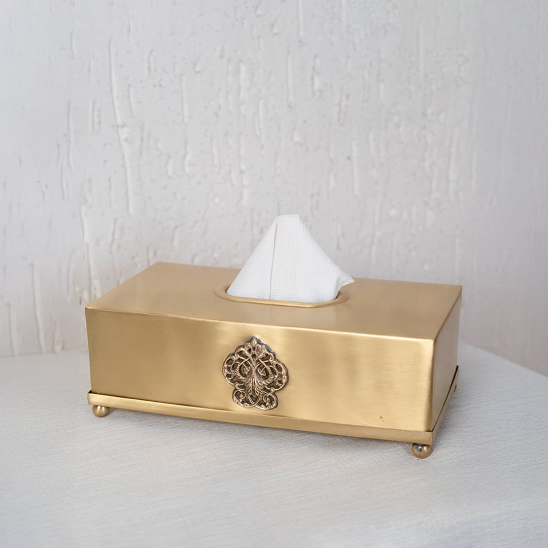 Gold tissue box holder partially covered with black branded packaging box on white background showing luxury style.