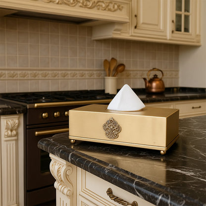 A gold tissue box with an elegant design displayed on a marble kitchen counter adding a refined touch to a classic interior with warm polished decor.