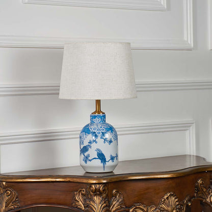 Blue and white patterned ceramic lamp with a beige lampshade displayed unlit against a clean white backdrop.