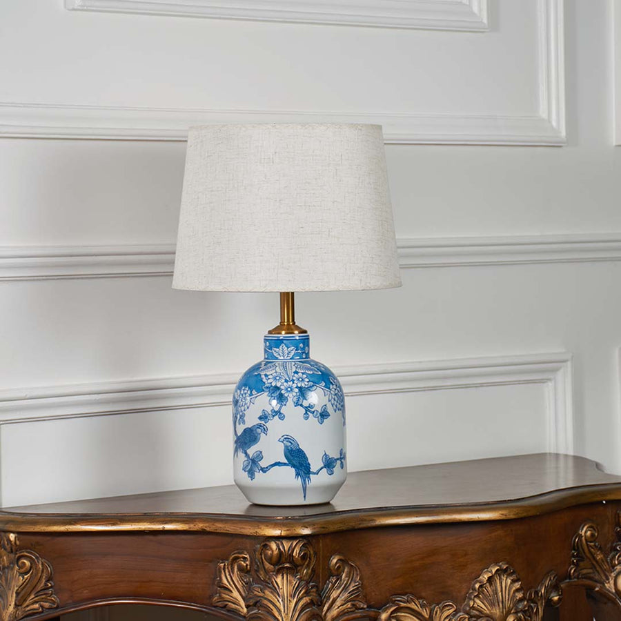 Blue and white patterned ceramic lamp with a beige lampshade displayed unlit against a clean white backdrop.