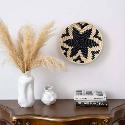 Decorative setup with a woven wall basket, pampas grass in a vase, and books on a wooden surface.