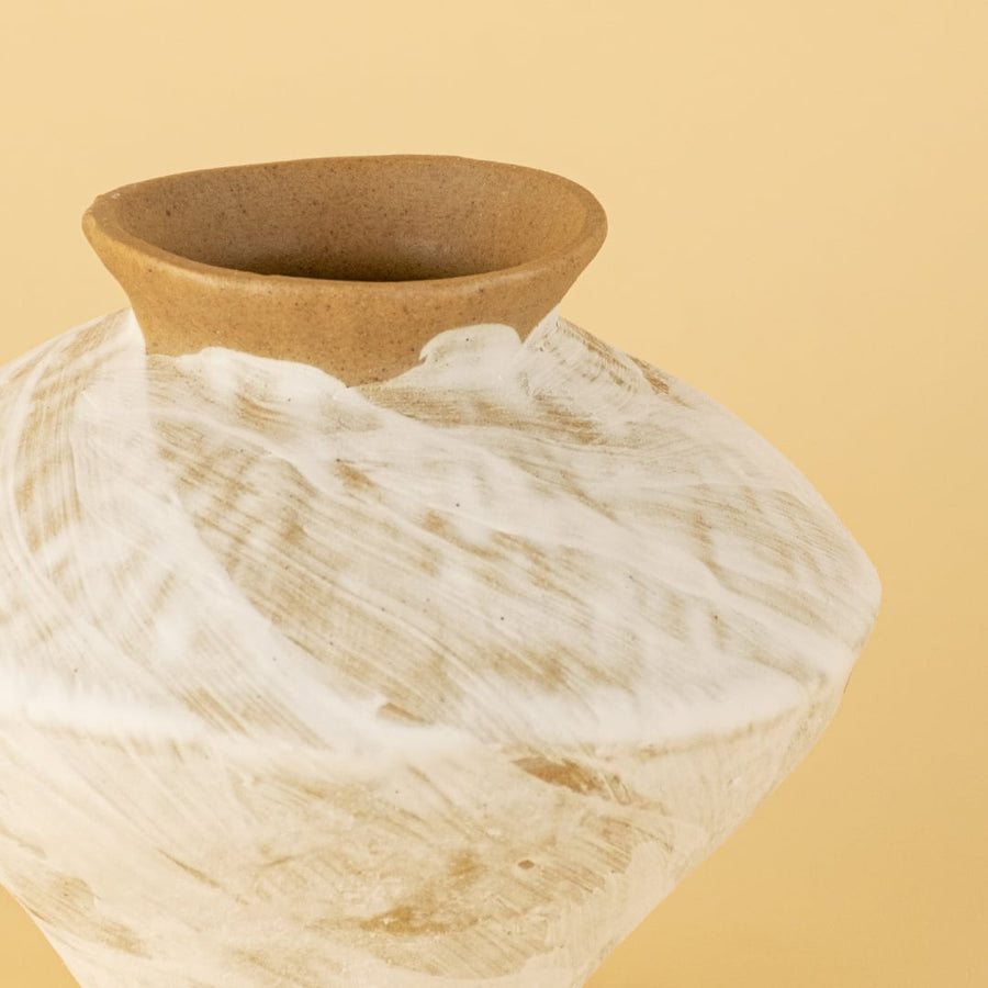 Closeup of handcrafted ceramic vase showing earthy brown rim and white brushed texture with natural clay tones on a soft warm yellow background.