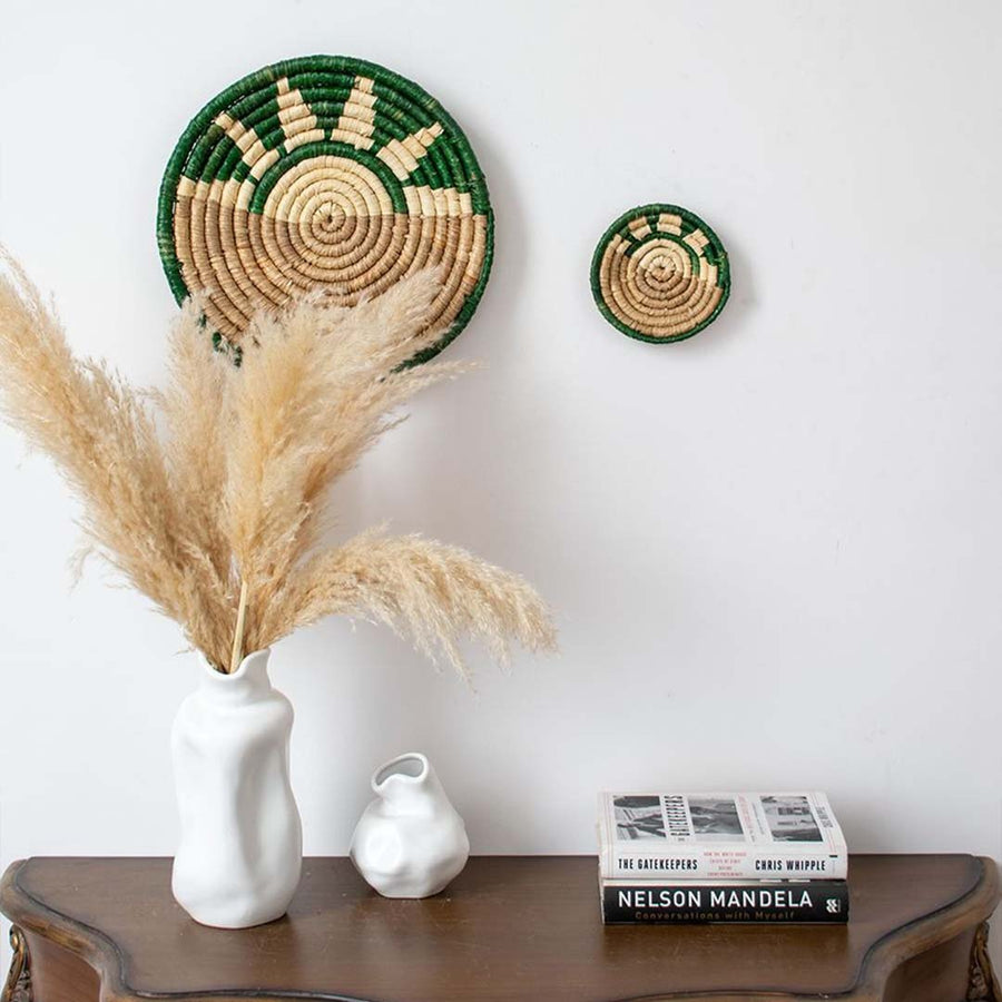 Green and beige bamboo wall plates styled above wooden table with white vase creating earthy natural home decor.