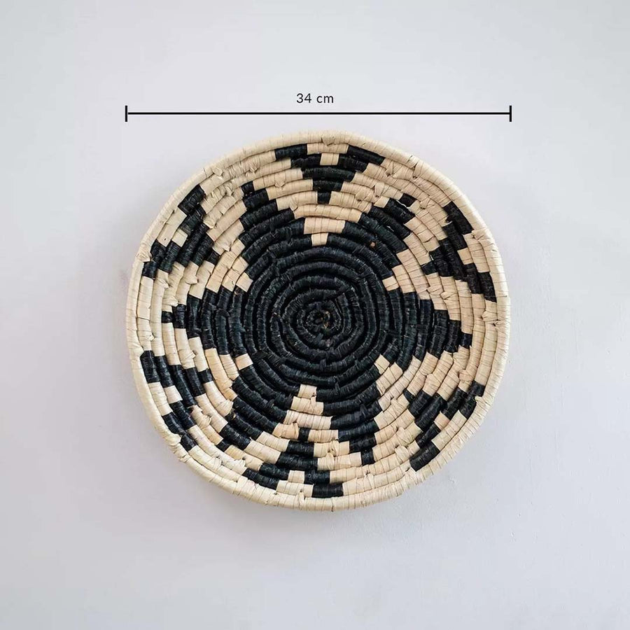 Handwoven round wall basket in natural and black fiber showing 30 cm diameter suitable for accent wall Decor placement indoors.