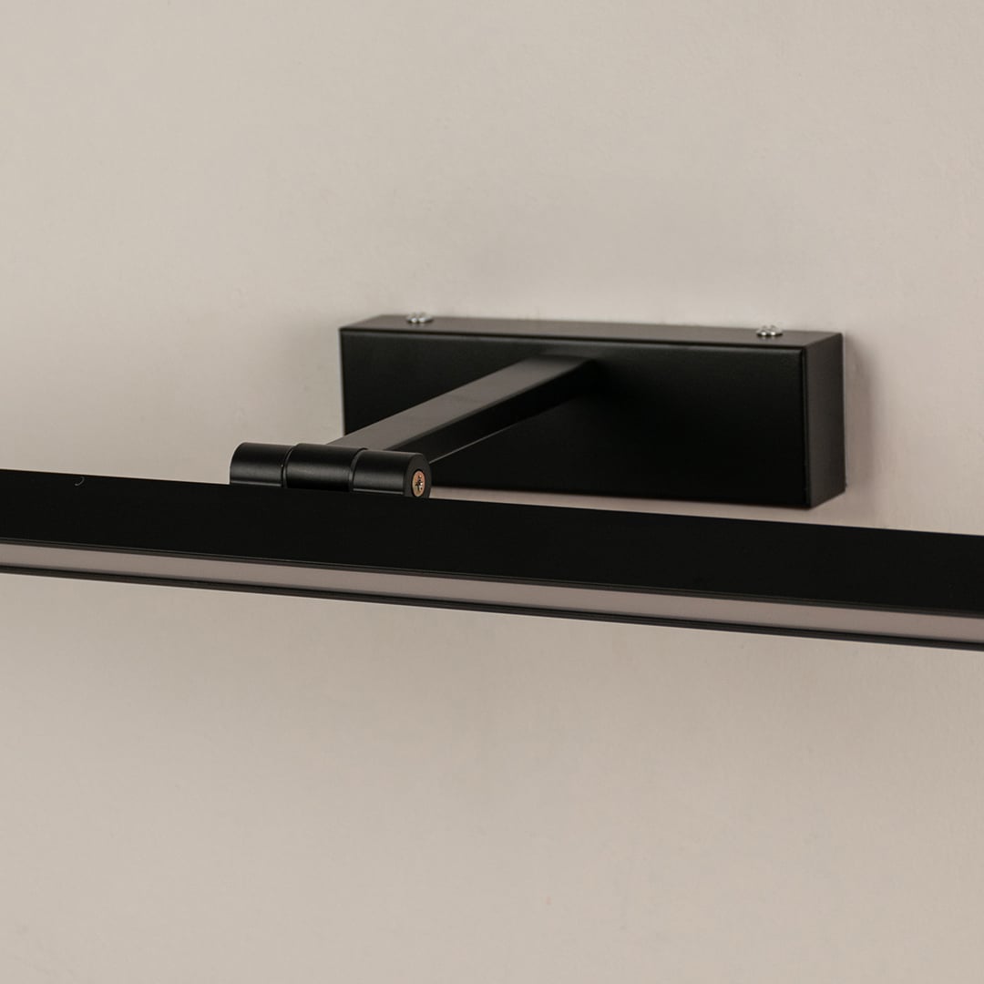 Closeup of black metal picture light showing slim bar design smooth finish and warm directional illumination.