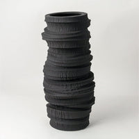 Black textured ceramic vase with stacked organic ring design placed on white surface against neutral background showcasing bold sculptural modern home decor styling.