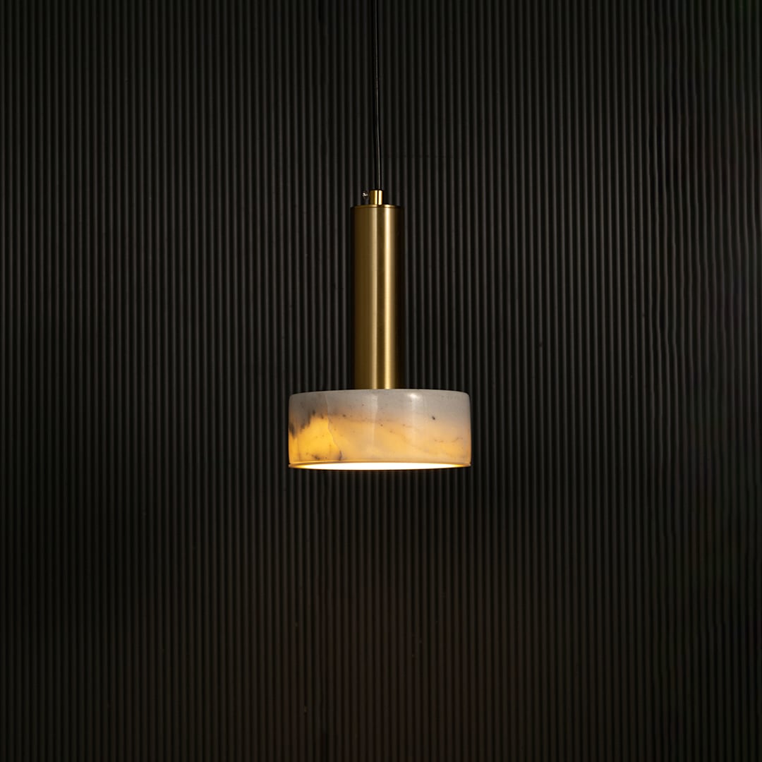 White marble and metal round base pendant light hanging against dark textured wall with light on for elegant contemporary décor.