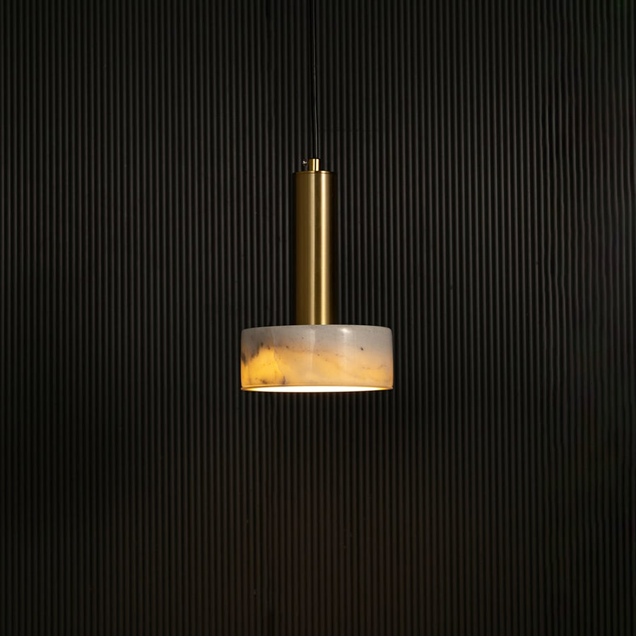 White marble and metal round base pendant light hanging against dark textured wall with light on for elegant contemporary décor.